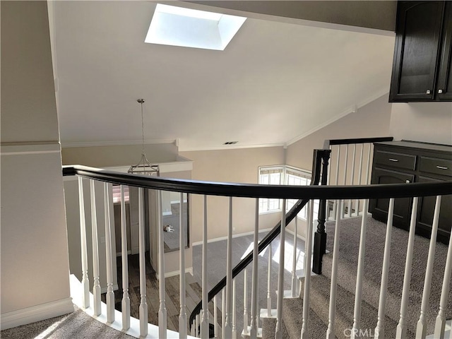 stairway featuring a chandelier, carpet, lofted ceiling with skylight, and crown molding
