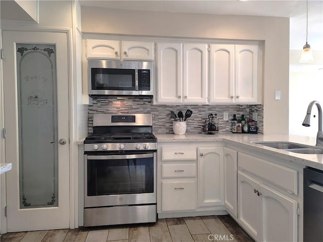 kitchen featuring stainless steel appliances, backsplash, a sink, white cabinetry, and light wood-type flooring