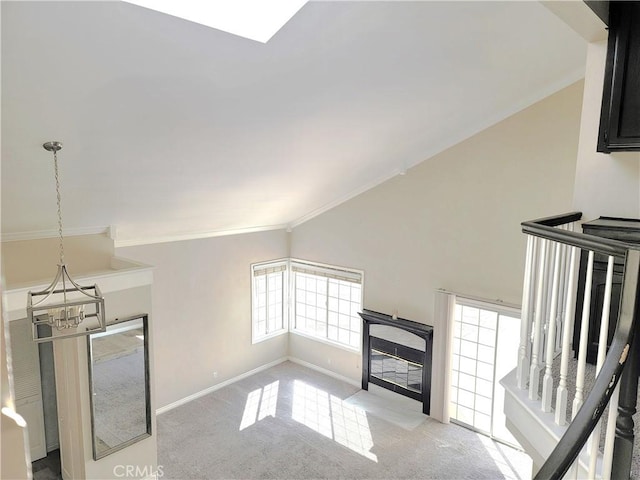 interior space featuring a fireplace with flush hearth, baseboards, carpet floors, vaulted ceiling, and a notable chandelier