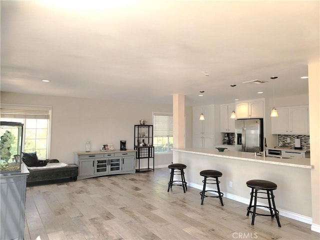 kitchen with a breakfast bar, stainless steel refrigerator with ice dispenser, light wood-style flooring, and light countertops