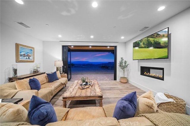 living room with recessed lighting, a glass covered fireplace, visible vents, and wood finished floors