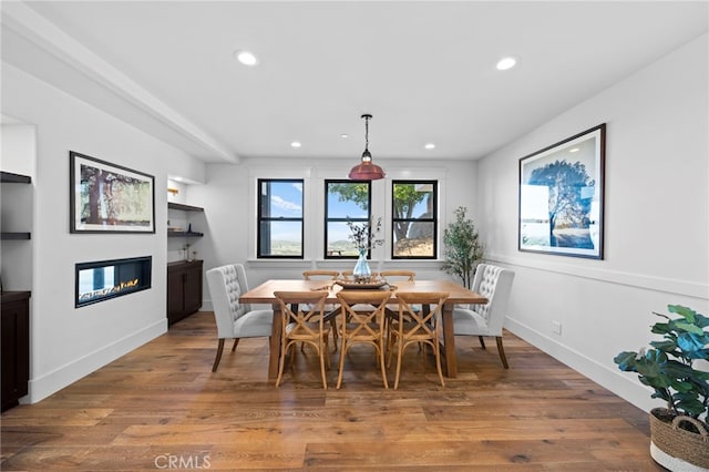 dining area featuring recessed lighting, built in features, a glass covered fireplace, and wood finished floors
