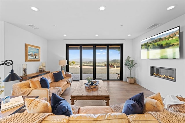 living room featuring recessed lighting, visible vents, a glass covered fireplace, and wood finished floors