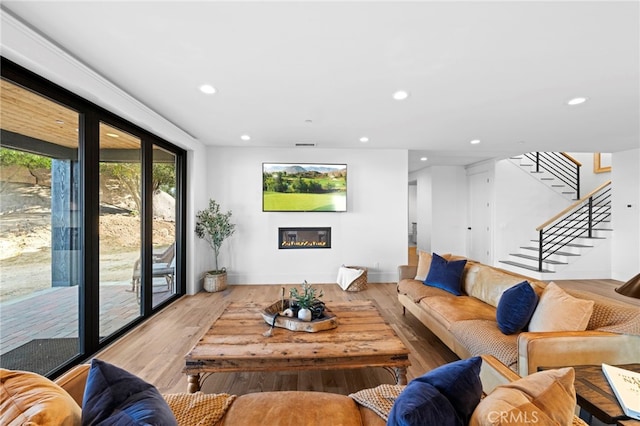 living area featuring wood finished floors, stairway, baseboards, a glass covered fireplace, and recessed lighting