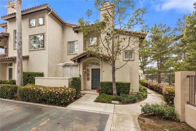 townhome / multi-family property featuring a chimney, a tile roof, fence, and stucco siding