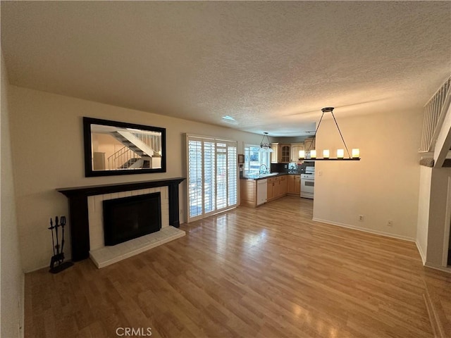 21643 Spice Ct, Saugus, CA 91350 - unfurnished living room featuring a tiled fireplace, light wood-type flooring, a textured ceiling, and a chandelier