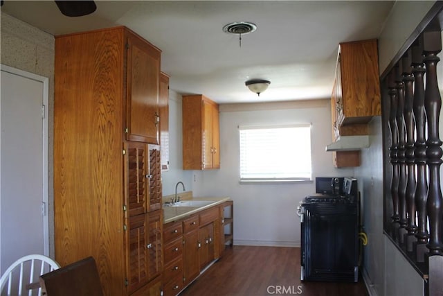 kitchen featuring a sink, brown cabinetry, black microwave, light countertops, and dark wood finished floors