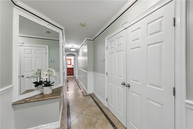 hall featuring arched walkways, light tile patterned flooring, crown molding, and baseboards