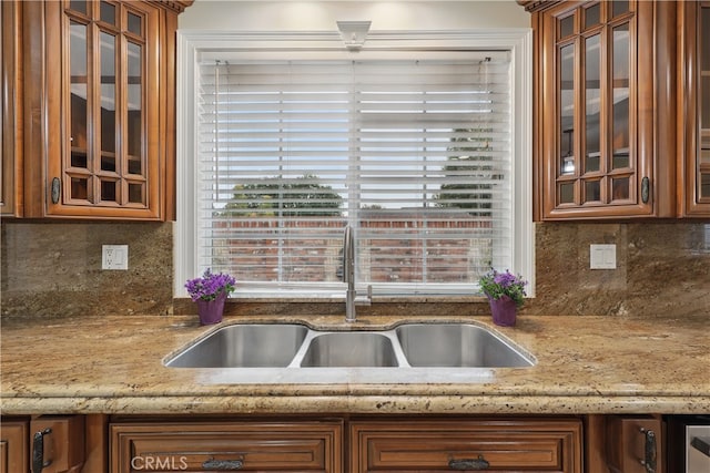 kitchen featuring decorative backsplash, brown cabinetry, a sink, and glass insert cabinets