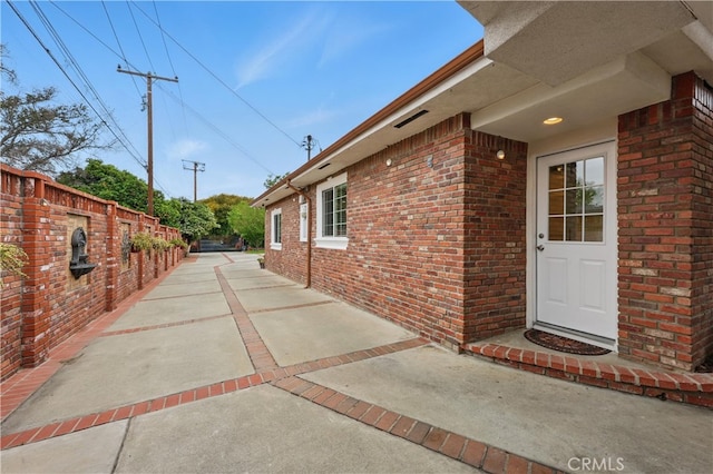 view of side of home featuring fence, a patio area, and brick siding