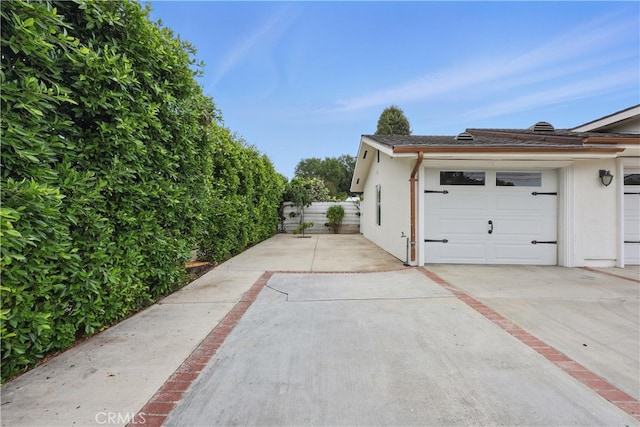 view of property exterior with driveway, stucco siding, and fence