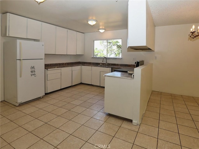 kitchen with dark countertops, a sink, light tile patterned floors, white cabinets, and freestanding refrigerator