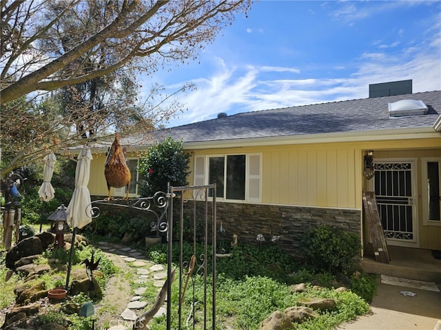 view of side of home featuring stone siding and a shingled roof