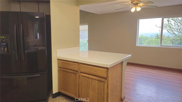 kitchen featuring brown cabinets, a ceiling fan, black refrigerator with ice dispenser, baseboards, and a peninsula