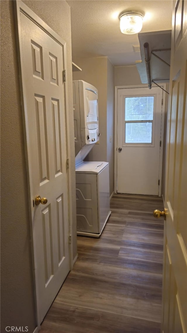 clothes washing area featuring dark wood-type flooring, stacked washer and clothes dryer, and laundry area