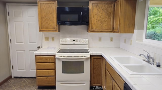 kitchen with white electric range oven, tile counters, a sink, brown cabinetry, and black microwave