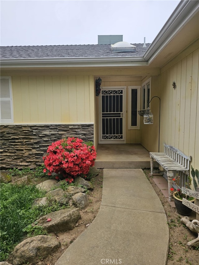 view of exterior entry with stone siding and a shingled roof