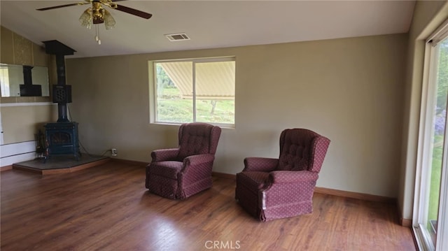 living area featuring visible vents, baseboards, wood finished floors, ceiling fan, and a wood stove