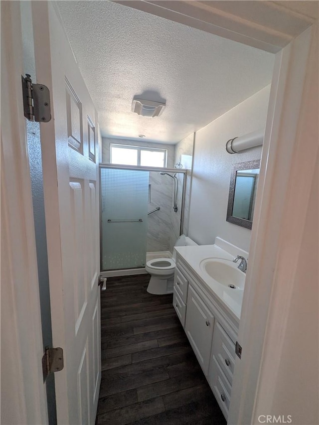 bathroom with a shower stall, wood finished floors, a textured ceiling, vanity, and toilet