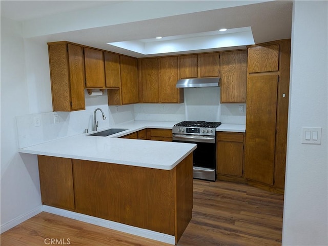 kitchen with a sink, brown cabinetry, a peninsula, under cabinet range hood, and stainless steel gas range oven