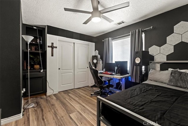 bedroom featuring a closet, a ceiling fan, visible vents, a textured ceiling, and wood finished floors