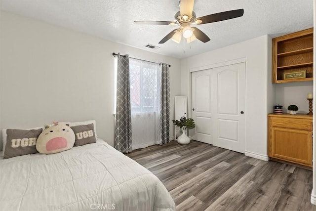 bedroom with dark wood-type flooring, visible vents, a textured ceiling, and a closet