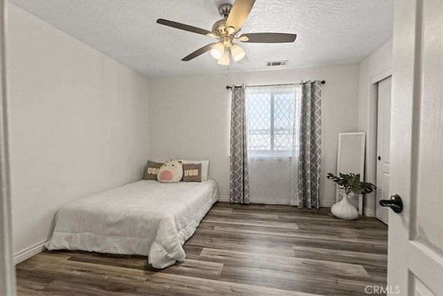 bedroom with a textured ceiling, visible vents, wood finished floors, and baseboards