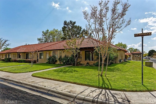 ranch-style home featuring a front lawn, a tiled roof, and stucco siding