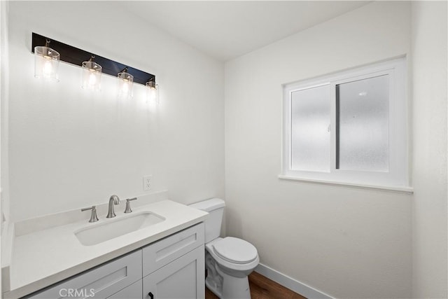 half bathroom featuring wood finished floors, vanity, toilet, and baseboards