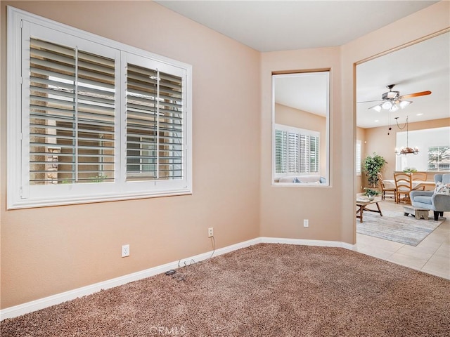 carpeted spare room with tile patterned flooring, baseboards, and ceiling fan with notable chandelier