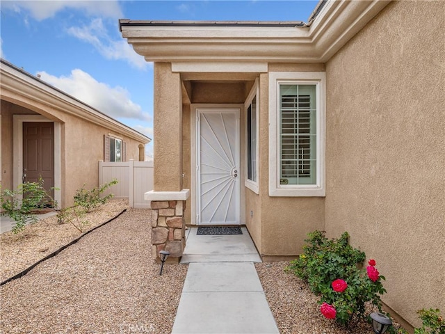 view of exterior entry featuring stucco siding and fence