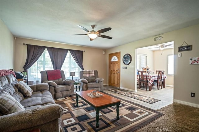 living area featuring baseboards, a ceiling fan, visible vents, and carpet