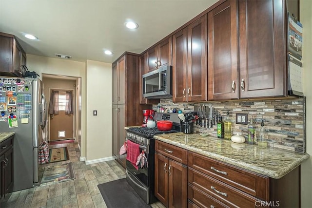 kitchen featuring light stone counters, decorative backsplash, stainless steel appliances, light wood finished floors, and visible vents