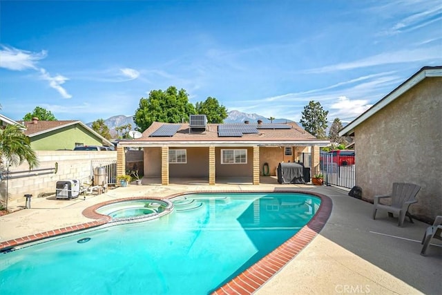 view of pool featuring fence, a patio area, a pool with connected hot tub, and a mountain view