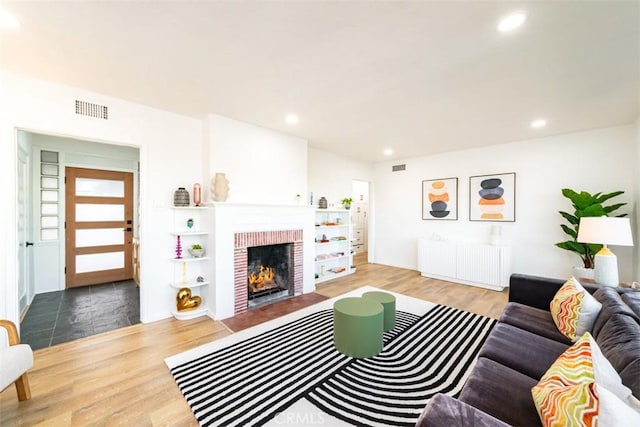 living room featuring radiator, recessed lighting, wood finished floors, visible vents, and a brick fireplace