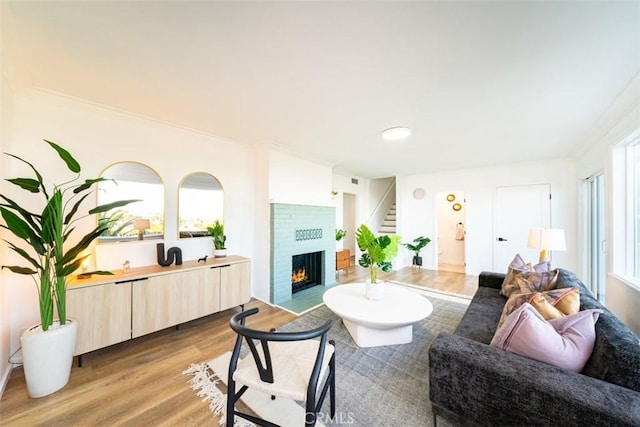 living area featuring light wood-type flooring, a brick fireplace, and ornamental molding