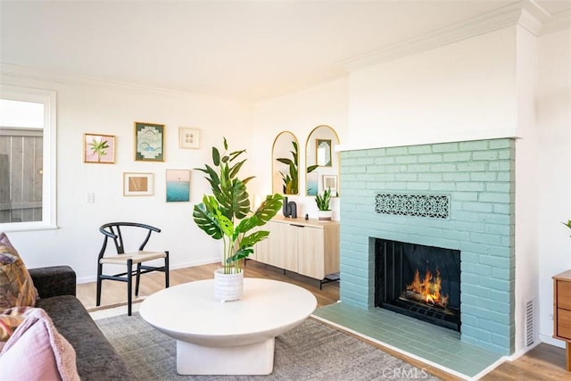 living area with visible vents, wood finished floors, a brick fireplace, and crown molding