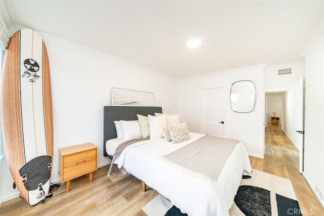 bedroom with light wood finished floors, baseboards, visible vents, and ornamental molding