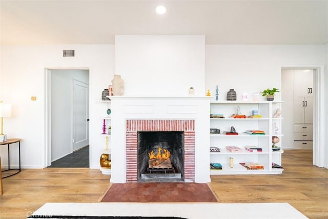 living area featuring visible vents, baseboards, recessed lighting, a brick fireplace, and wood finished floors