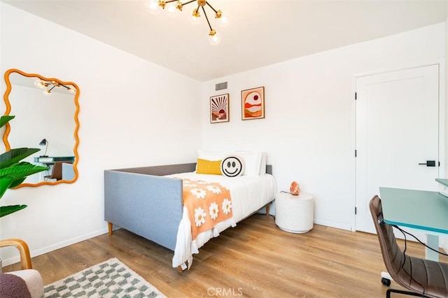 bedroom featuring wood finished floors, visible vents, baseboards, and an inviting chandelier