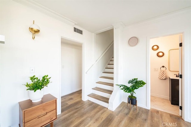 staircase featuring baseboards, wood finished floors, visible vents, and crown molding