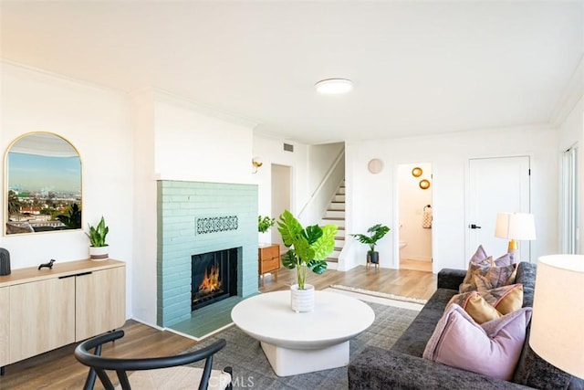 living area featuring crown molding, stairs, wood finished floors, a brick fireplace, and visible vents