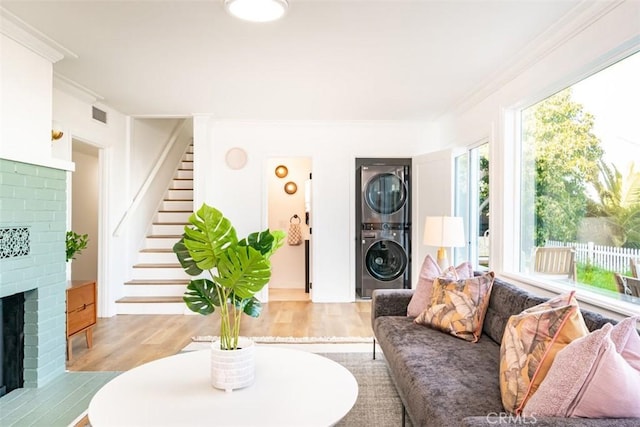 living room with stacked washer / dryer, wood finished floors, stairway, a fireplace, and ornamental molding