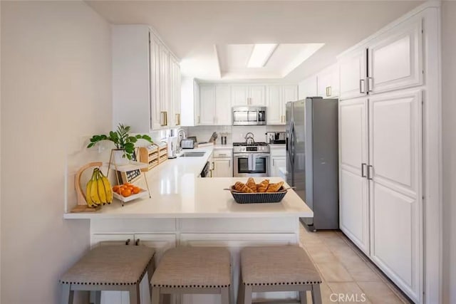 kitchen featuring stainless steel appliances, a sink, a peninsula, light countertops, and white cabinetry