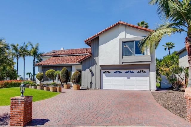 mediterranean / spanish home with a garage, a tiled roof, decorative driveway, and stucco siding