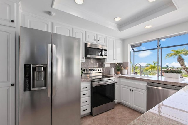 kitchen with white cabinets, a raised ceiling, a sink, crown molding, and appliances with stainless steel finishes
