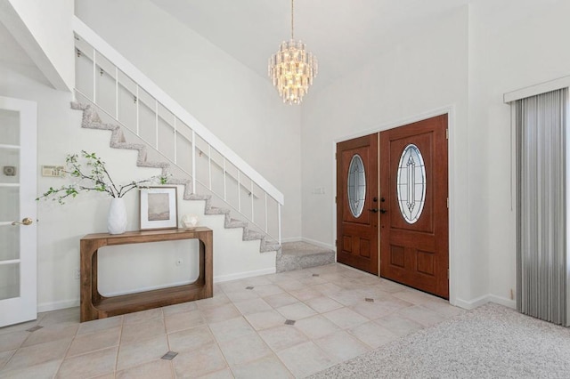 tiled entryway with baseboards, a towering ceiling, stairs, and an inviting chandelier