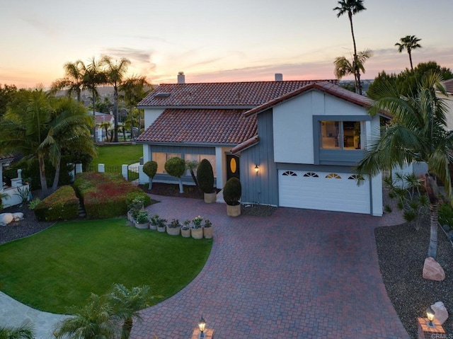 mediterranean / spanish-style home with a tile roof, decorative driveway, a garage, a chimney, and a front yard