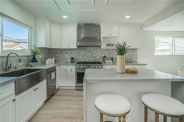 kitchen with wall chimney exhaust hood, a kitchen breakfast bar, a sink, recessed lighting, and appliances with stainless steel finishes