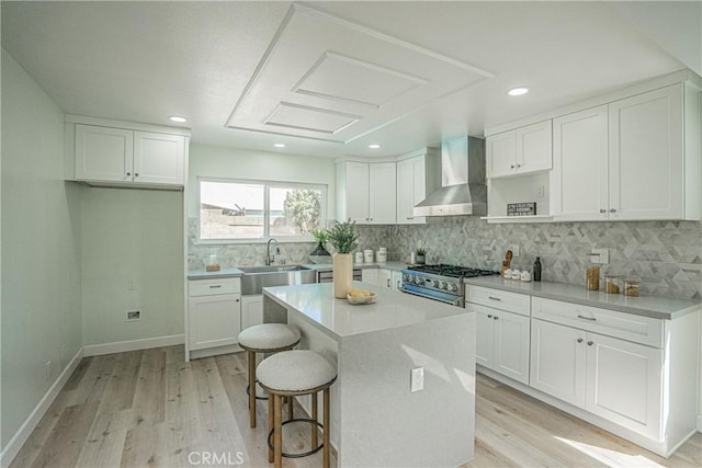 kitchen featuring a sink, high end range, light wood-type flooring, wall chimney exhaust hood, and white cabinetry